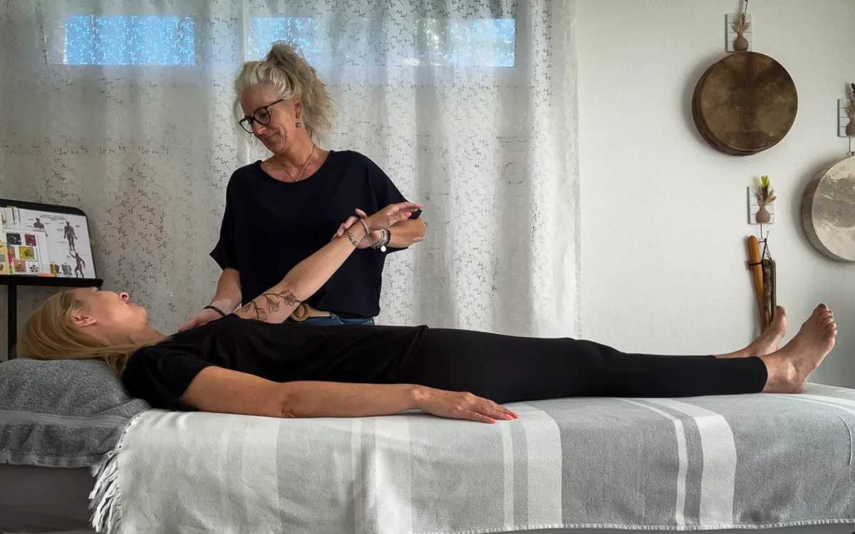 Kinesiologie-Sitzung in der Praxis: Nicole f&uuml;hrt einen sanften Muskeltest am Arm einer entspannt liegenden Klientin durch.
